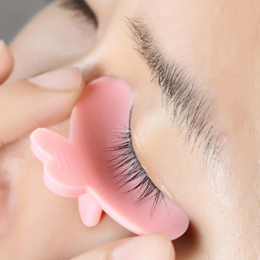 Pink YSEN’S Step 1 reverse lash lift shield positioned along the upper lash line using the center handling tab