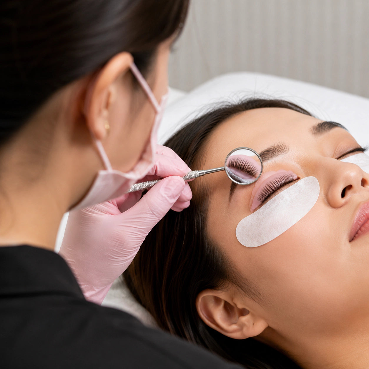 Lash artist using YSEN’S professional mirror to inspect eyelashes positioned on a pink lash lift shield